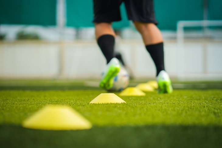 A footballer dribbling in between the cones